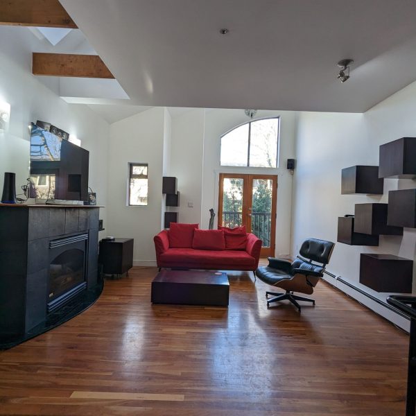 Modern living room with red sofa, hardwood floors, white walls, and vaulted ceiling with exposed beams and skylight.
