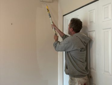 Experienced painter using extension roller to repaint beige wall, upgrading room with fresh color.
