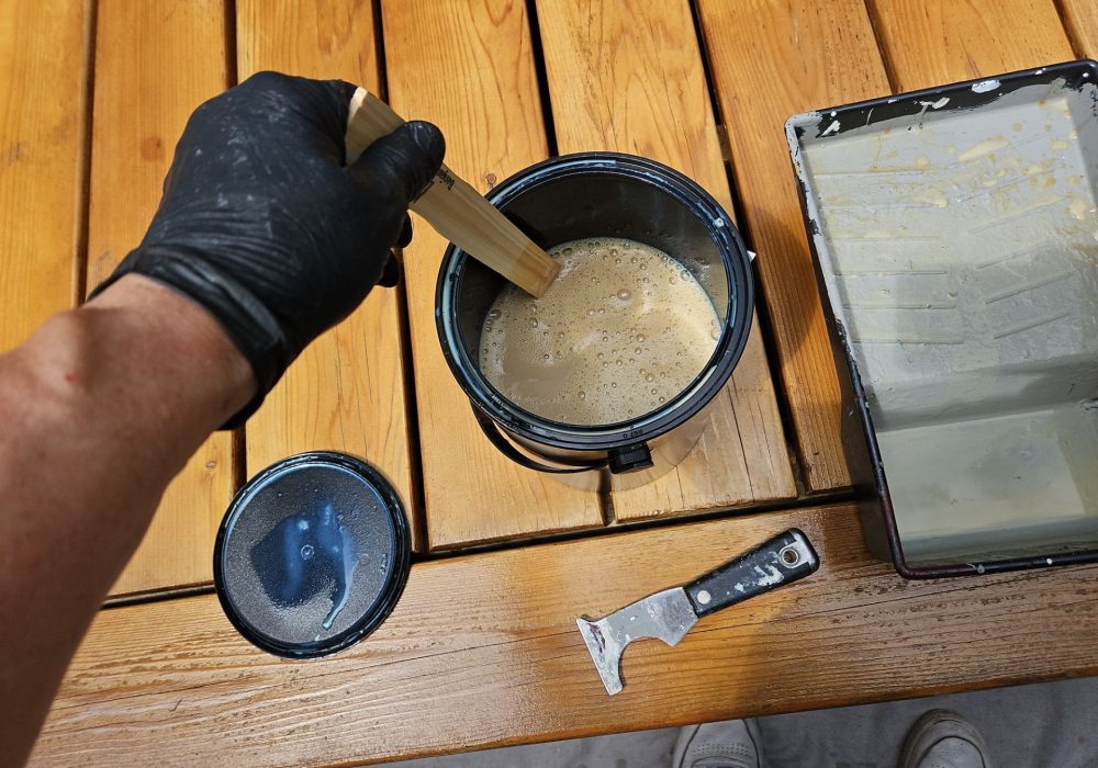 Person using paint brush on wooden deck table, deck repair tools