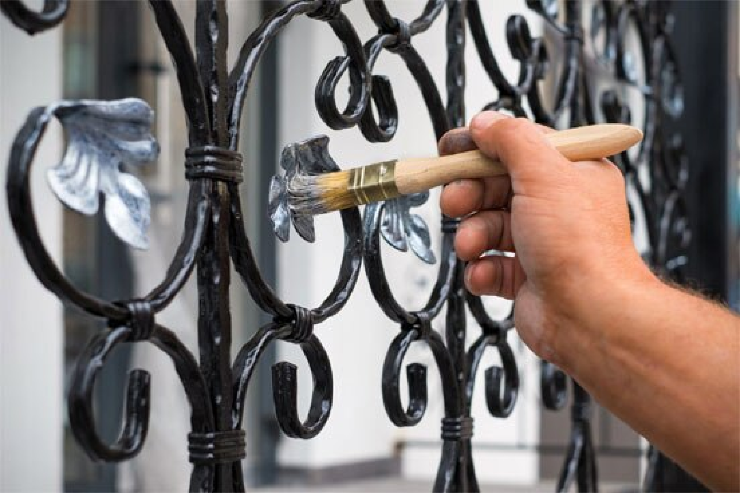 A painter is painting a metal fence with a brush.