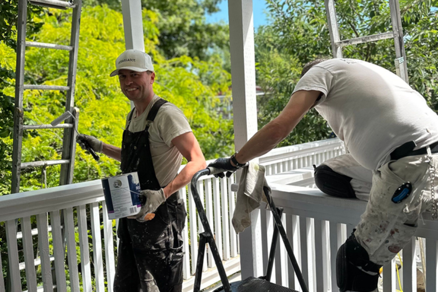 A couple of painter are painting a railing in a white colour with a painting materials in the middle.